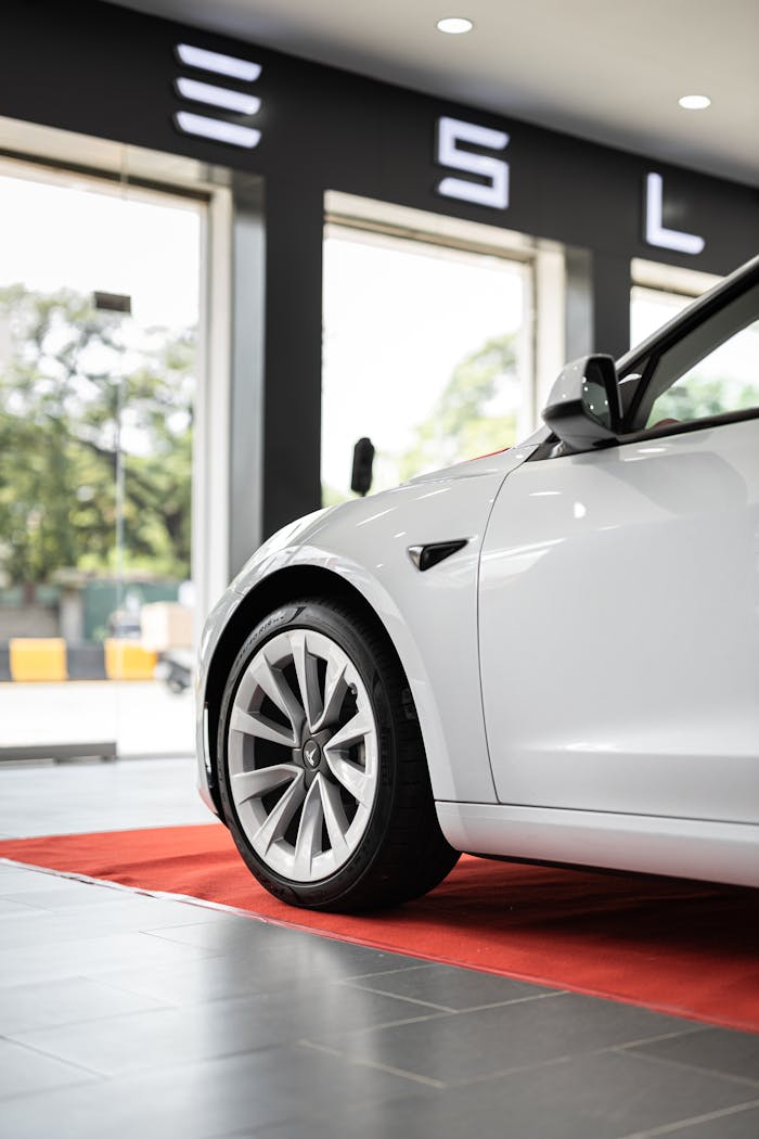 Close-up of a white electric car parked on a red carpet indoors, showcasing luxury and innovation.